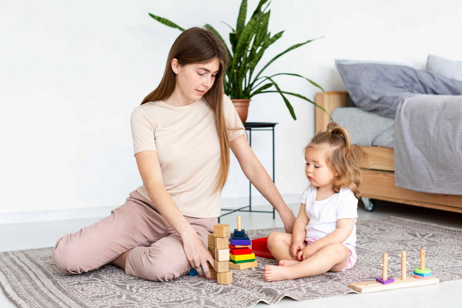 A woman and a toddler playing with a stacking toy on a rug at home